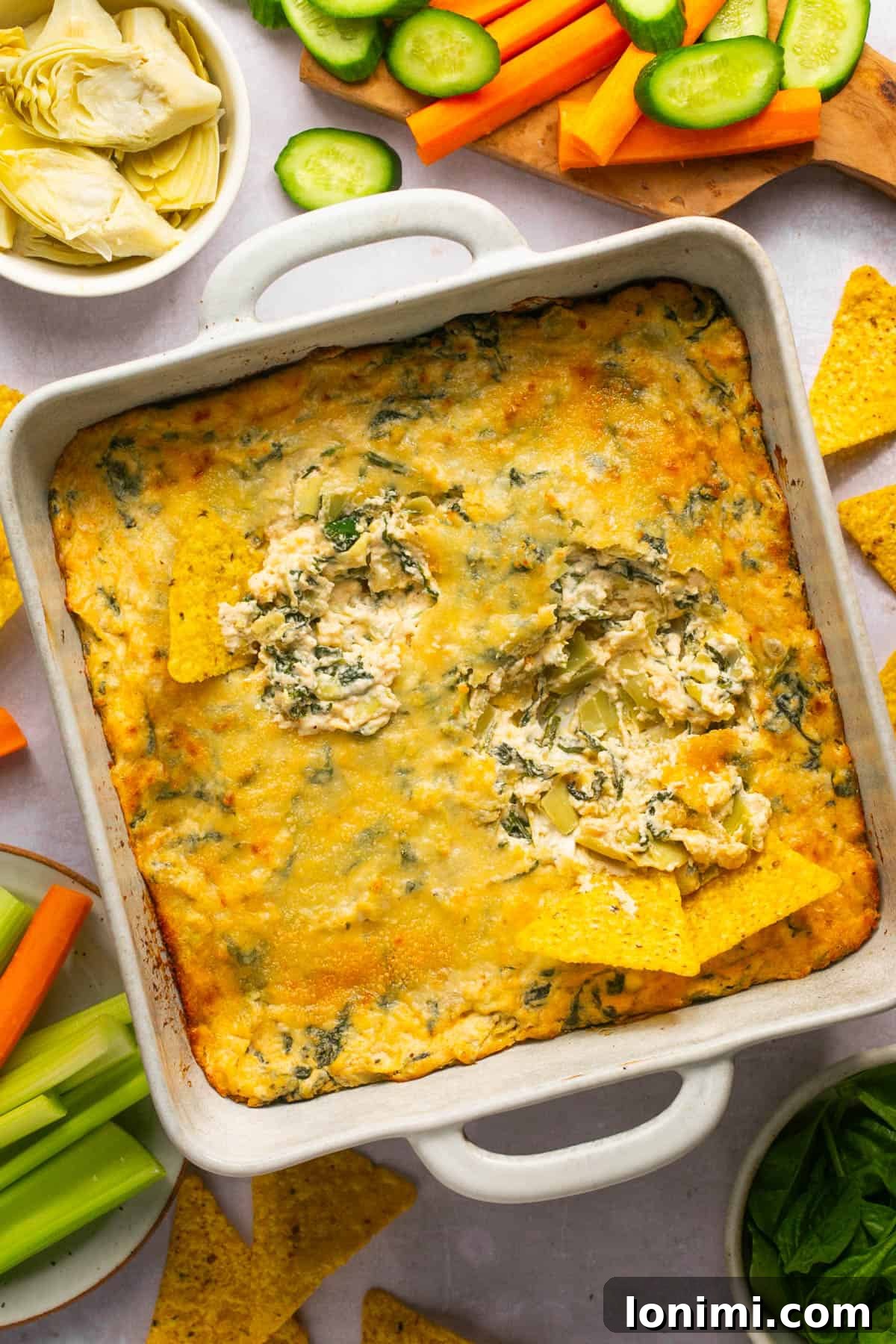 Decadent Mayo-Free Spinach Artichoke Dip 12 An overhead shot of no mayo spinach artichoke dip in a baking dish surrounded by various dippers