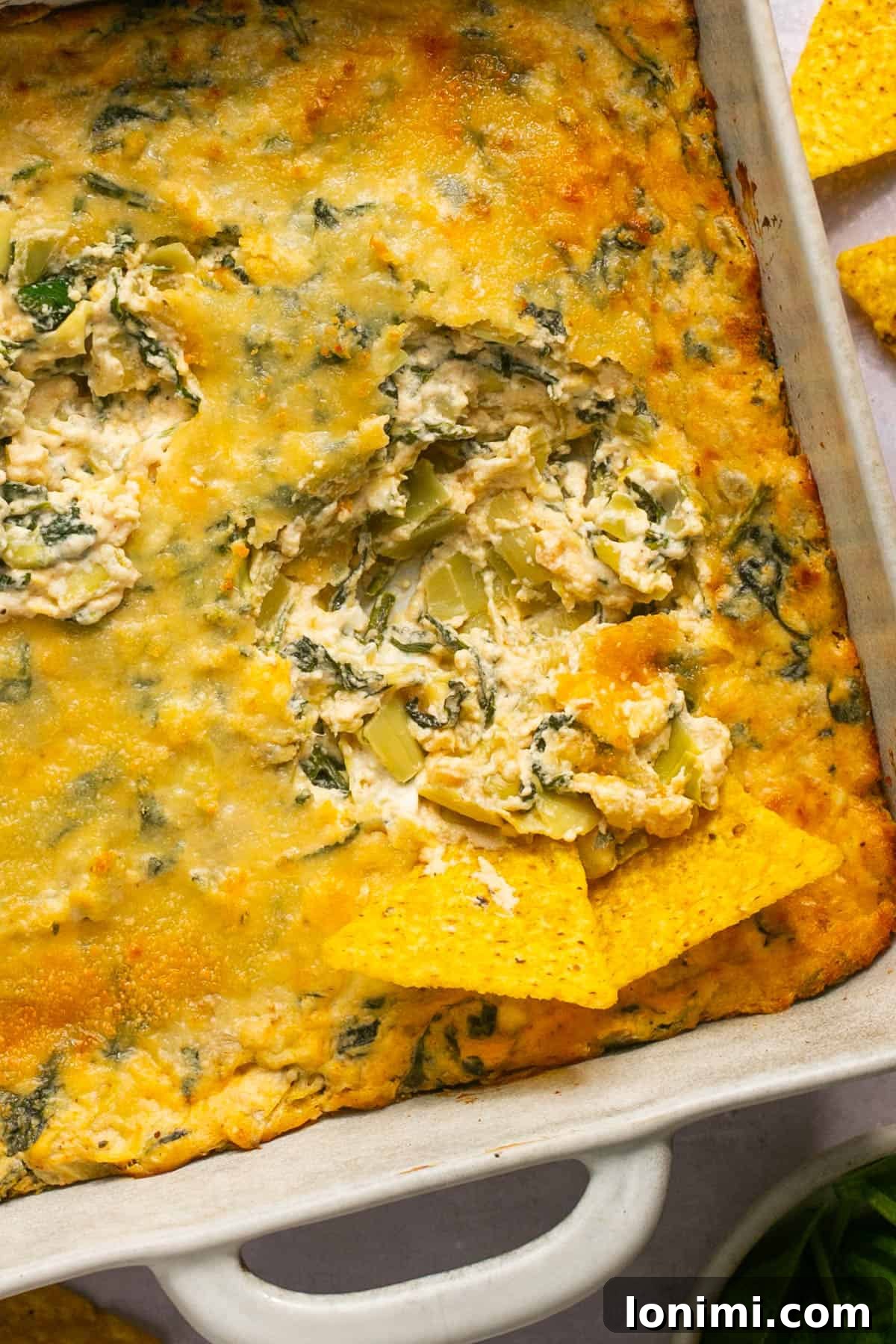 Decadent Mayo-Free Spinach Artichoke Dip 13 A close-up shot of no mayo spinach artichoke dip with two tortilla chips resting inside