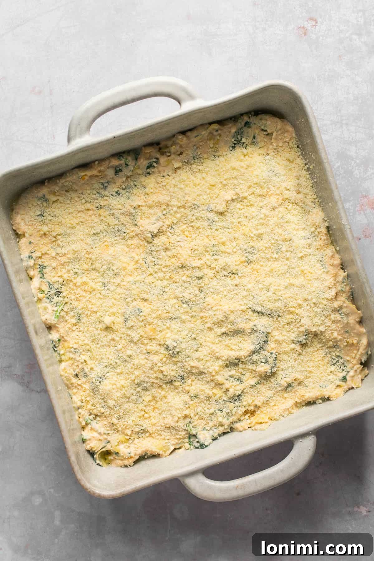 Decadent Mayo-Free Spinach Artichoke Dip 10 Spinach artichoke dip mixture spread into a 9x9 square baking dish, topped with Parmesan cheese