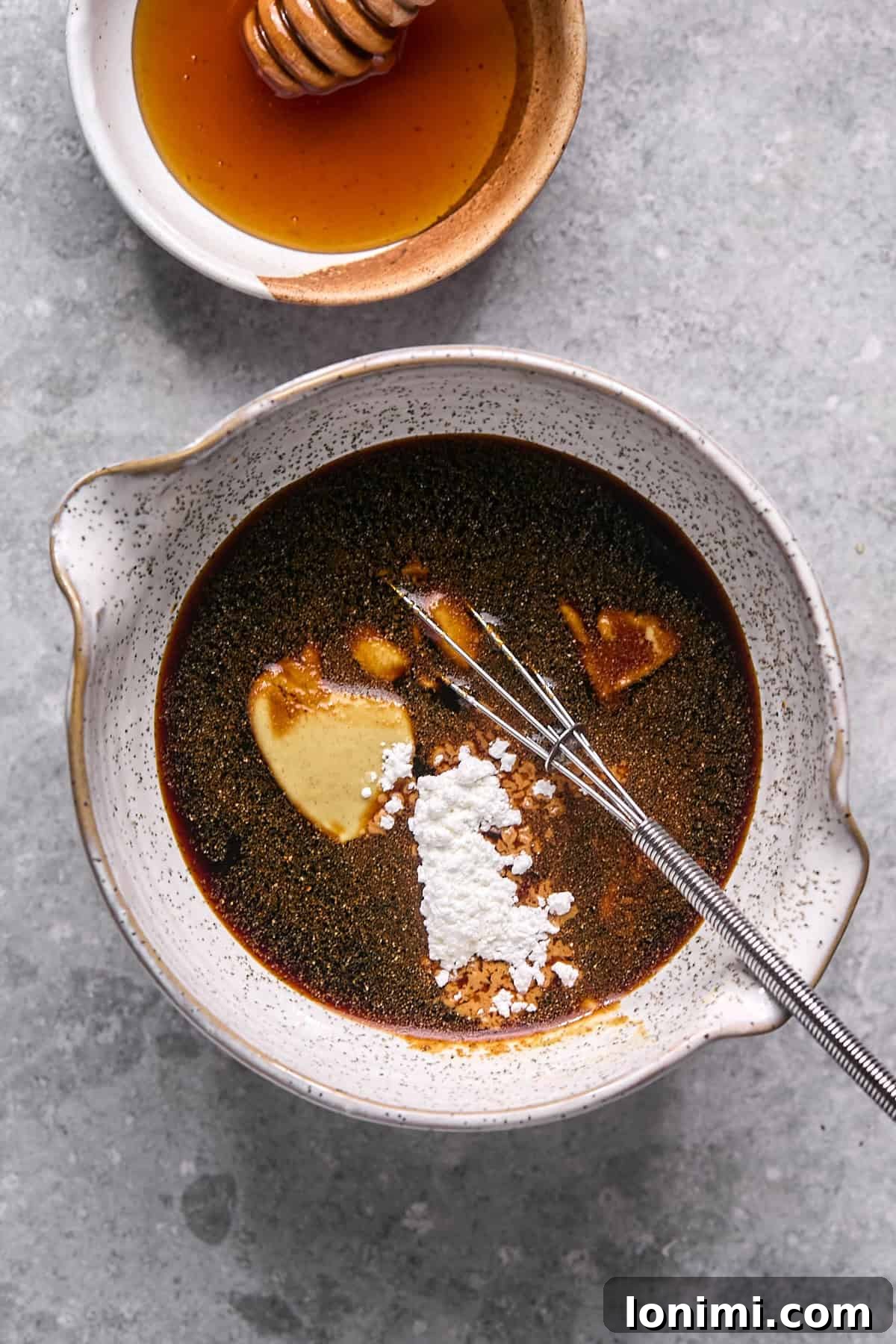 Gluten Free Hot Honey Glazed Shrimp and Sausage Stir Fry 4 Ingredients for hot honey sauce, including coconut aminos, Dijon mustard, and hot honey, being combined in a clear bowl with a whisk.