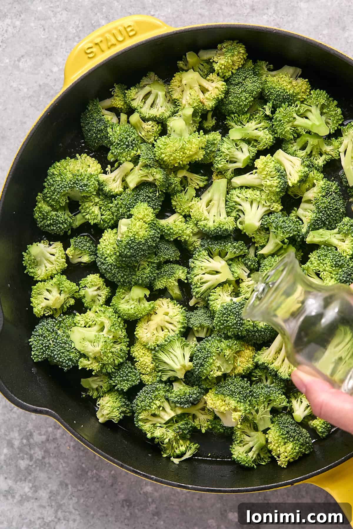 Gluten Free Hot Honey Glazed Shrimp and Sausage Stir Fry 8 Fresh broccoli florets in the skillet with a stream of water being poured in, preparing for steaming.