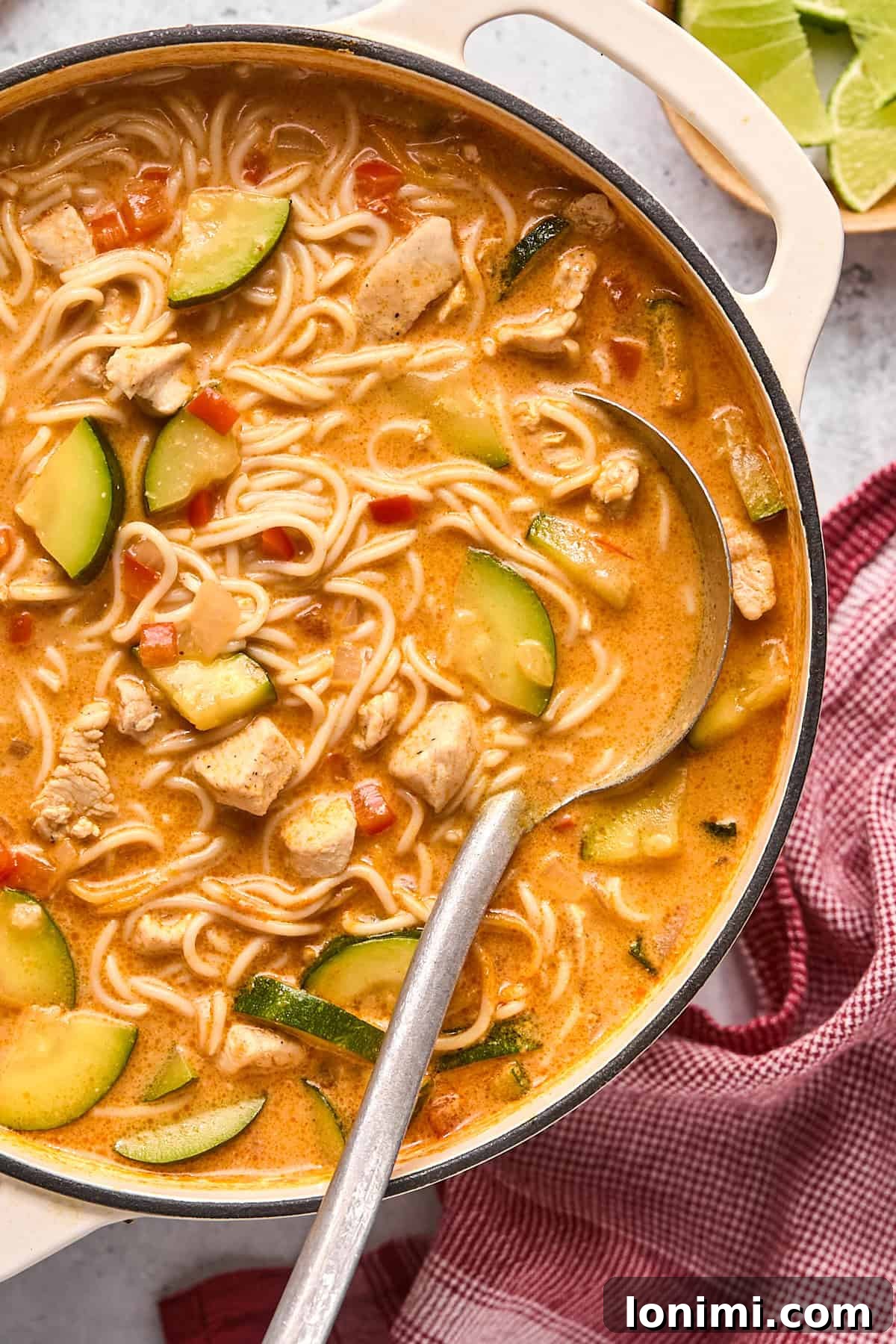 a close up shot of red curry soup in a large pot with a ladle