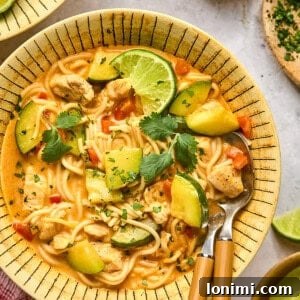 red thai curry noodle soup in a bowl with 2 wooden spoons