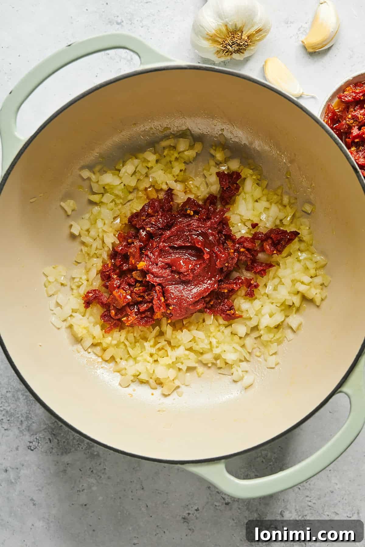 Sautéed onions, garlic, and vibrant sun-dried tomatoes stirred together in a pot, forming a rich base for the soup.