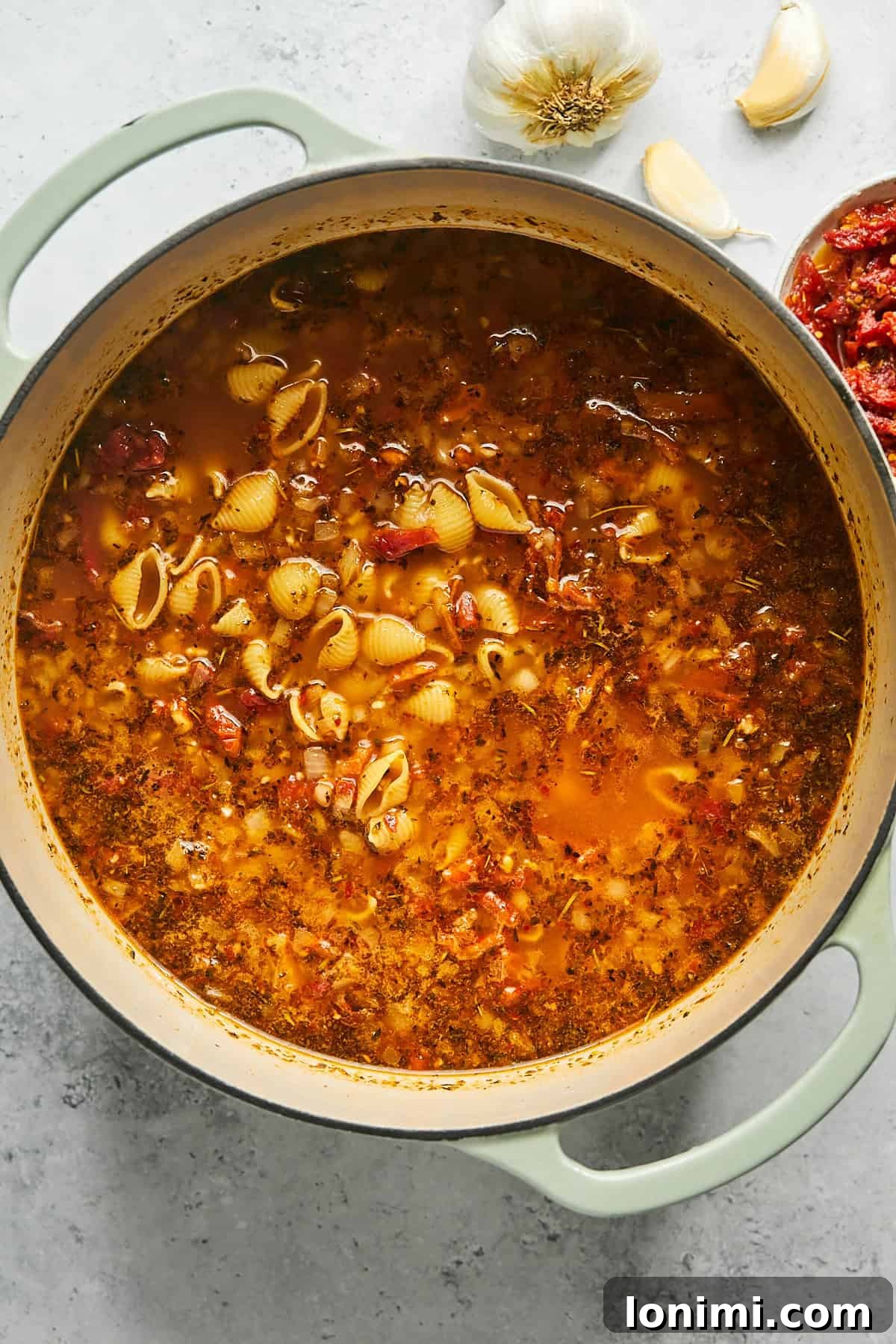 Gluten-free shell pasta cooking in the vibrant red broth, absorbing flavors and softening to an al dente texture.