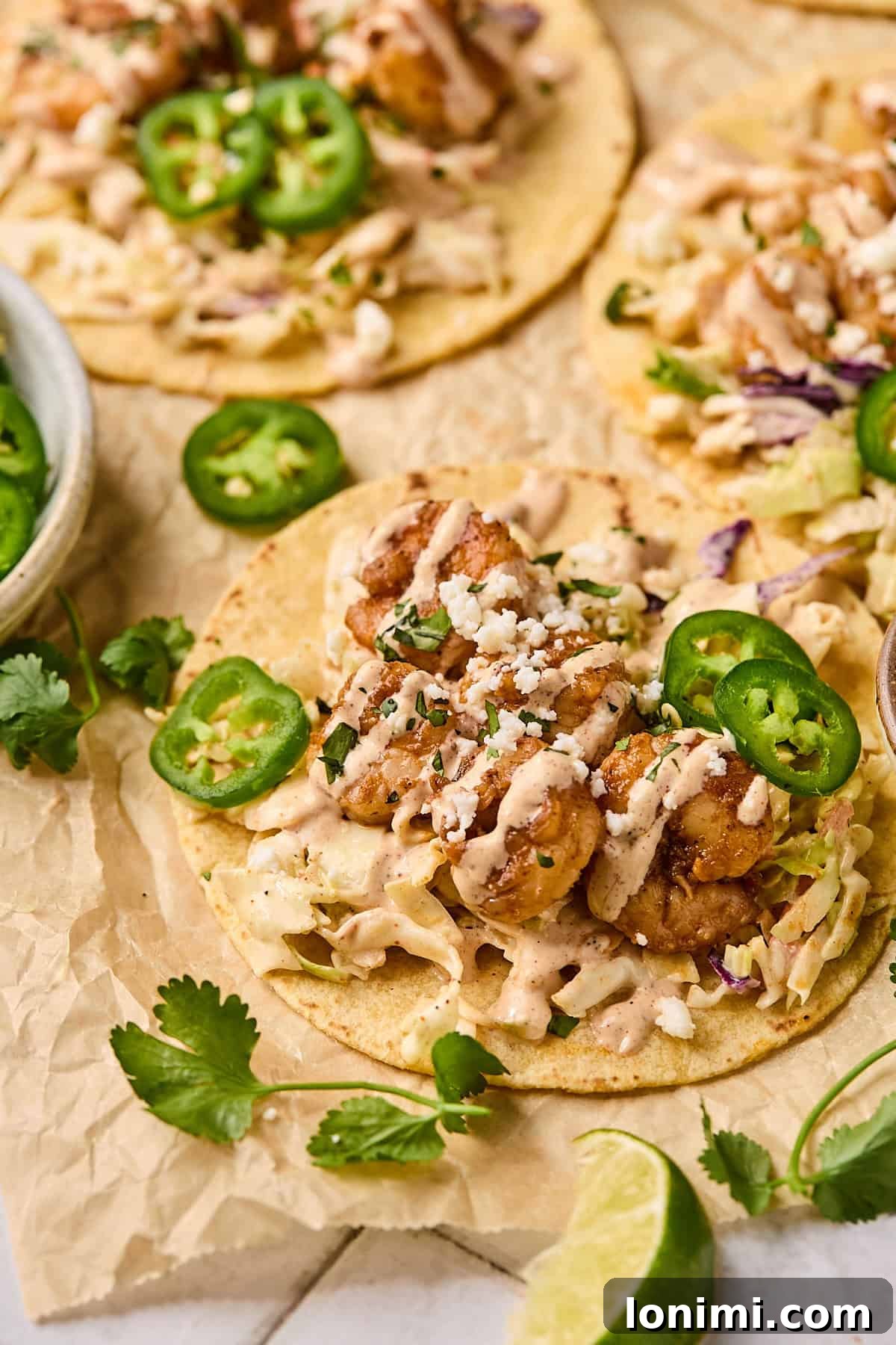 A close-up view of vibrant Baja shrimp tacos, generously topped with fresh jalapeno slices, crumbled cheese, and a creamy, zesty sauce.