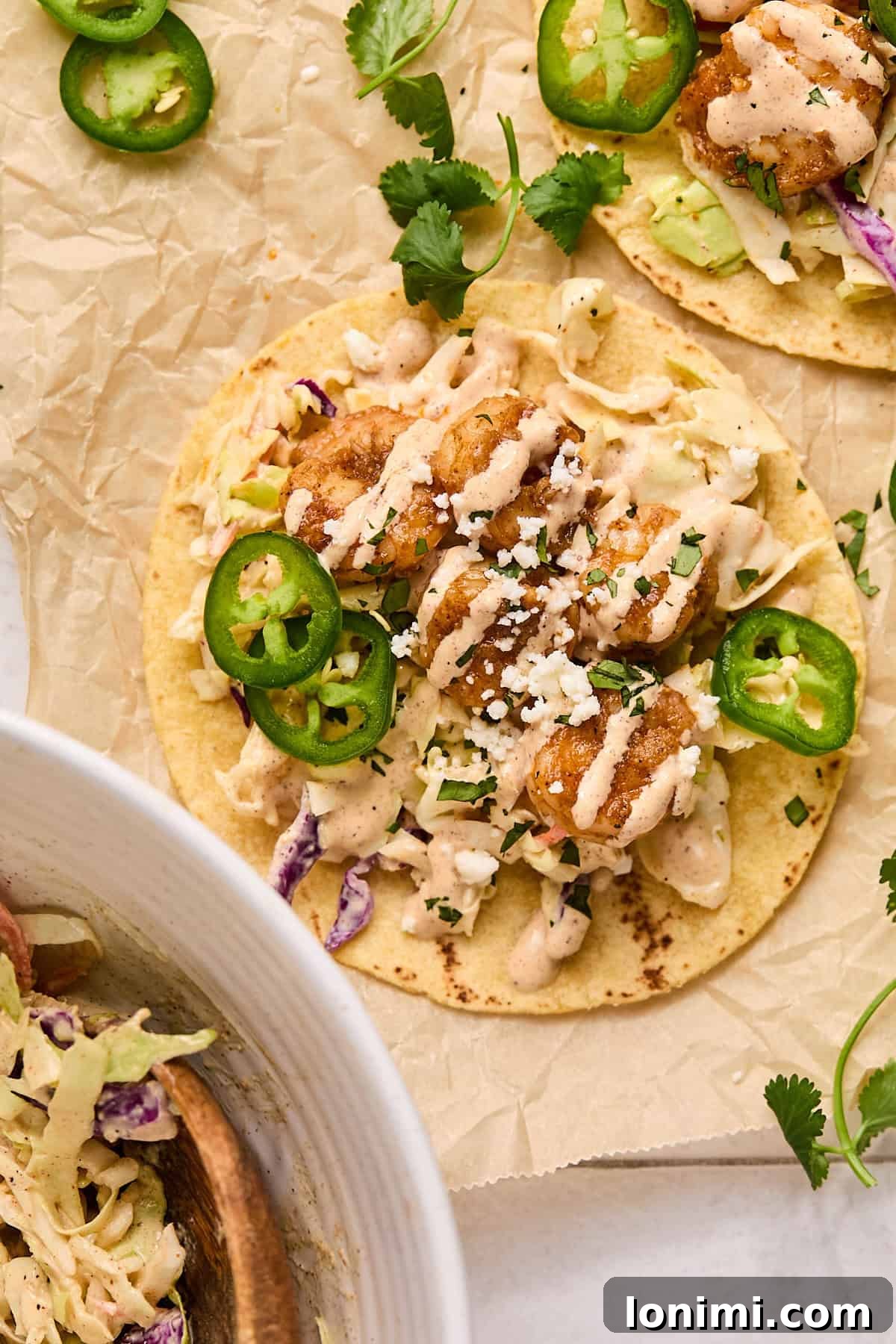 A fully assembled Baja shrimp taco, showcasing layers of seasoned shrimp, crisp slaw, creamy sauce, and fresh toppings, on parchment paper.