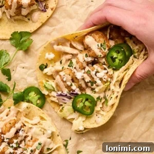 Baja shrimp tacos on parchment paper with a hand holding one, ready to be enjoyed.