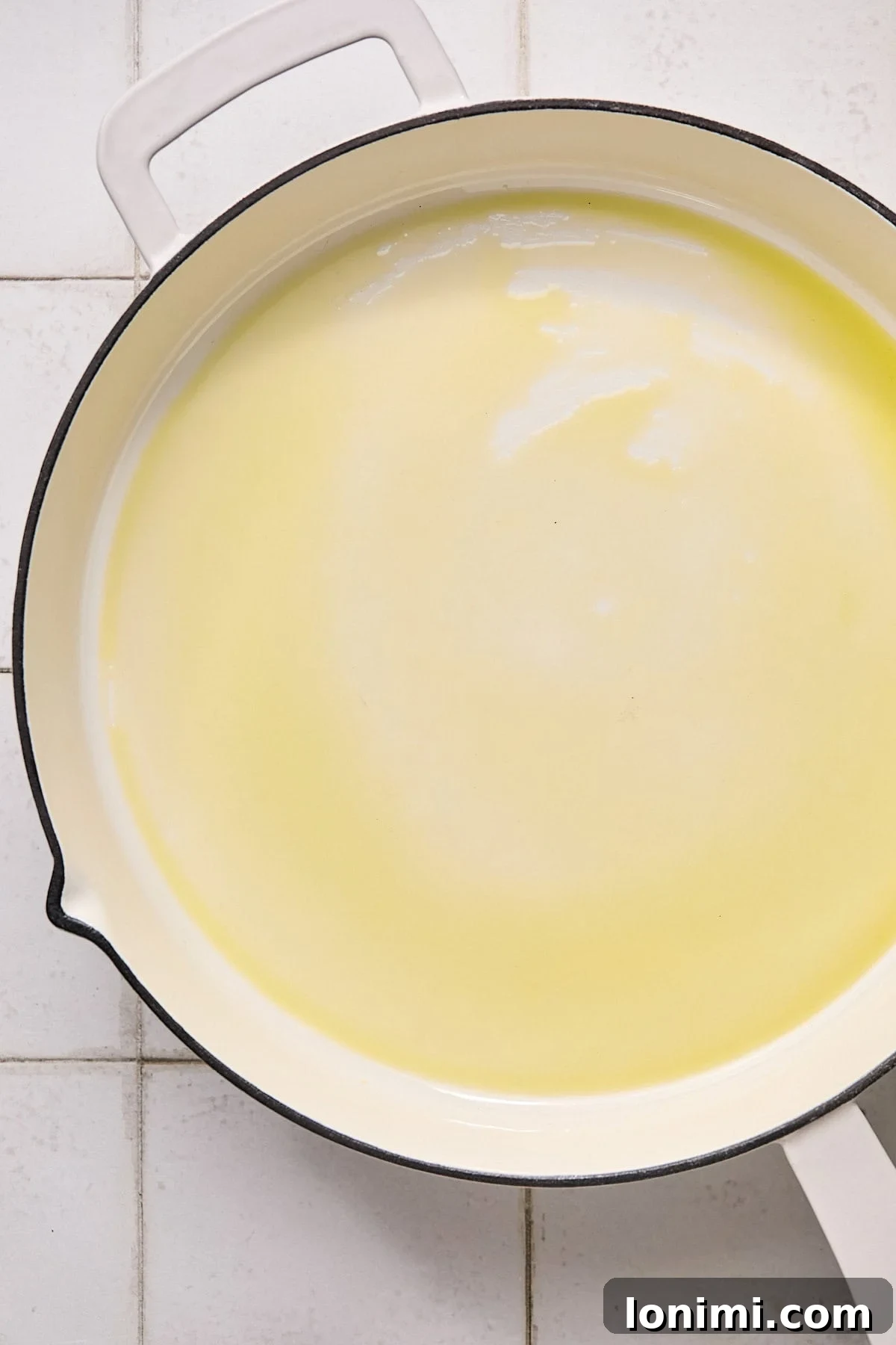 A white cast iron pan with a glistening pool of olive oil, ready for cooking.