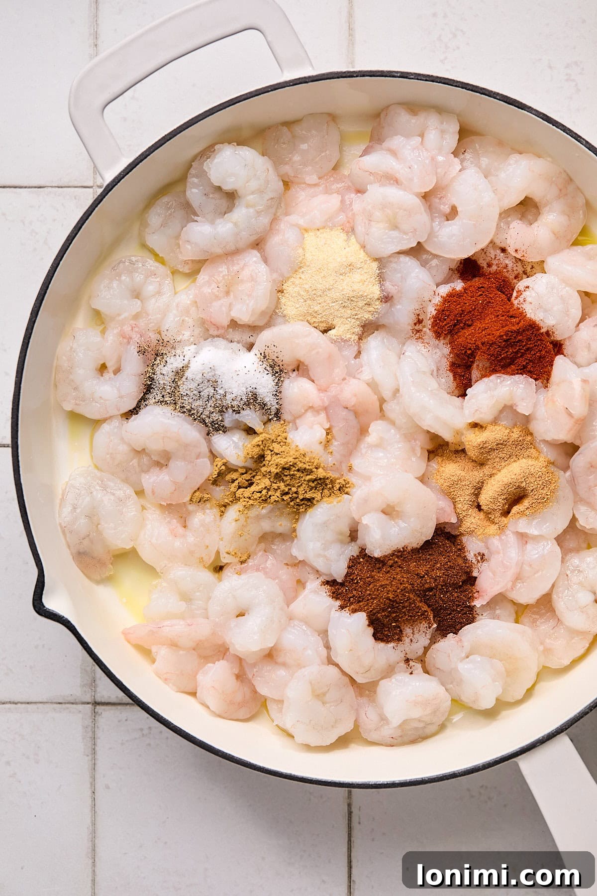 Raw, pink shrimp beautifully seasoned with a vibrant mix of spices, spread evenly in a pan, ready for cooking.