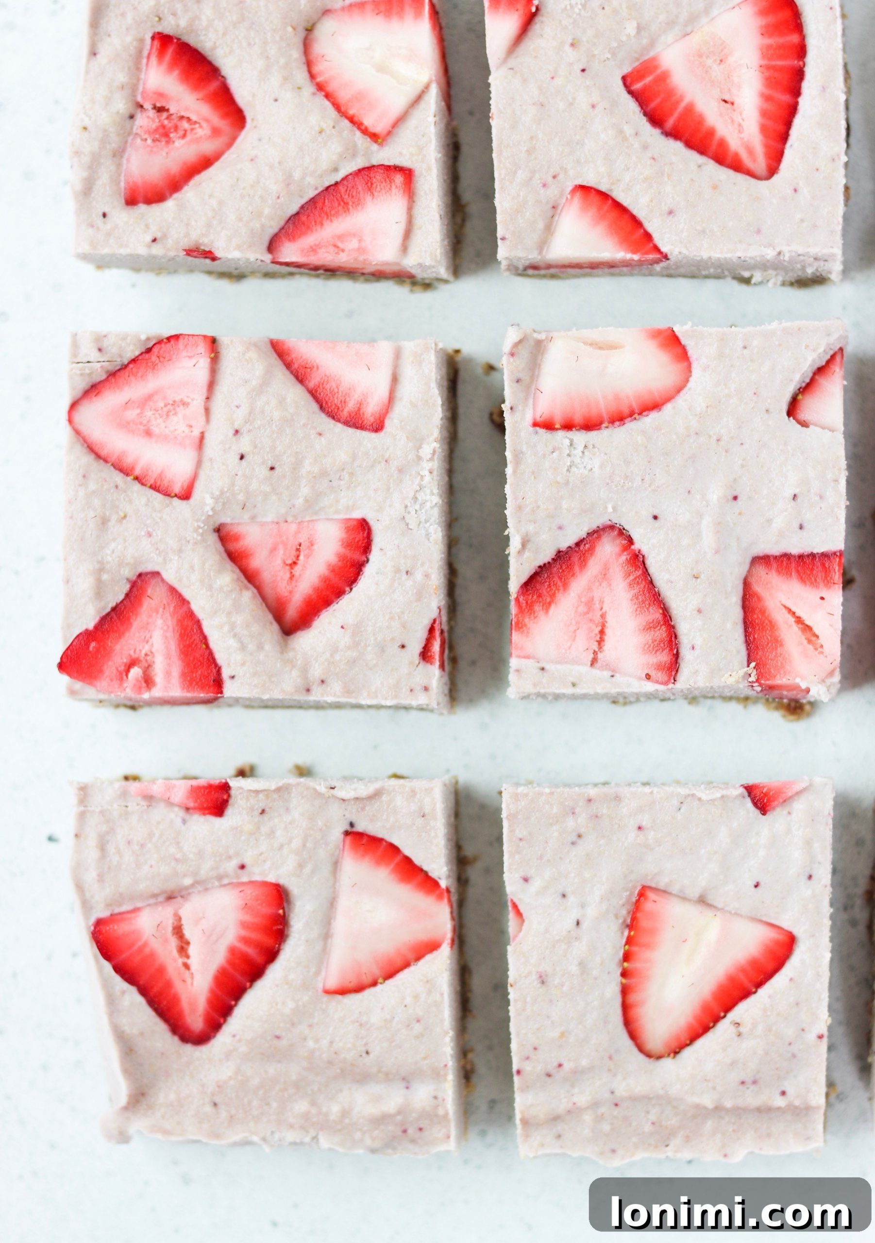 Delicious Paleo & Vegan No-Bake Strawberry Cheesecake Bars on a wooden board, garnished with fresh strawberries