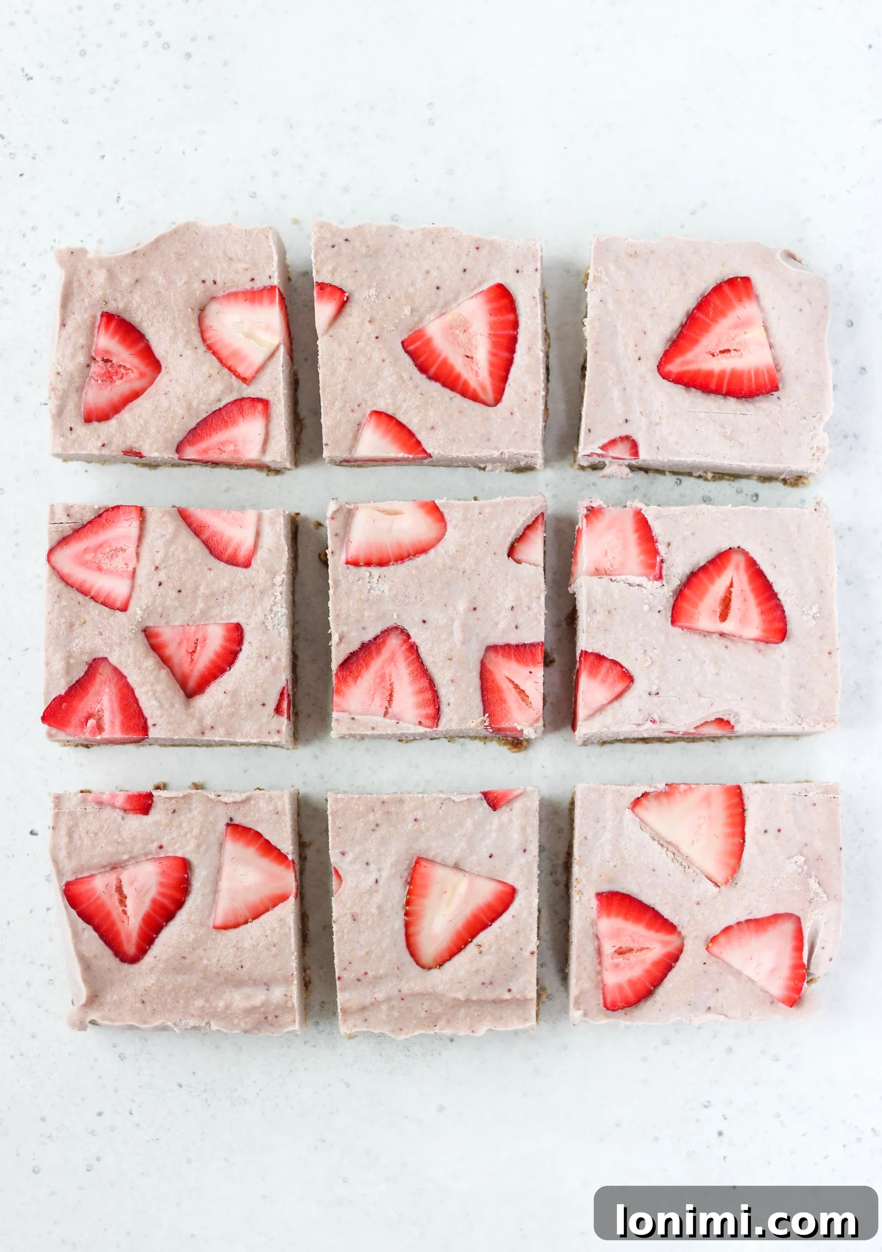 Finished Paleo & Vegan No-Bake Strawberry Cheesecake Bars, topped with fresh strawberries, ready to be sliced
