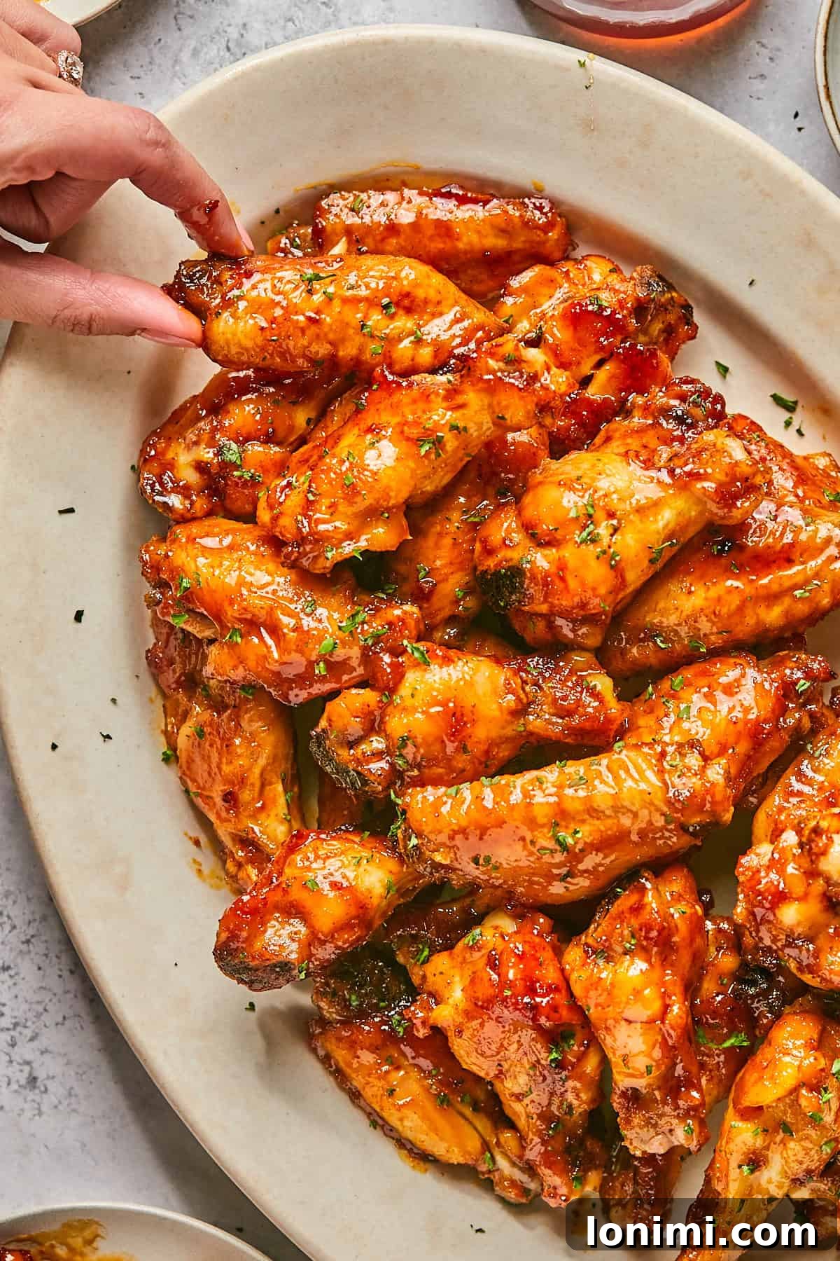 a hand holding a chicken wing from a platter of wings