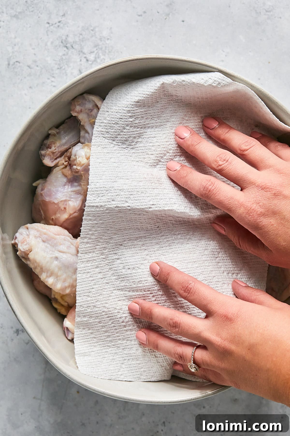 wings in a bowl with a hand using a paper towel to dry them off