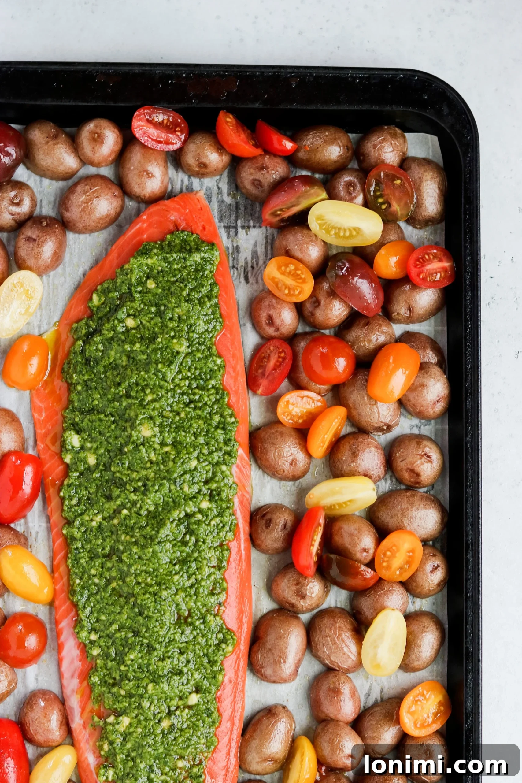 Full sheet pan meal of pesto salmon, roasted potatoes, and tomatoes, ready to serve.