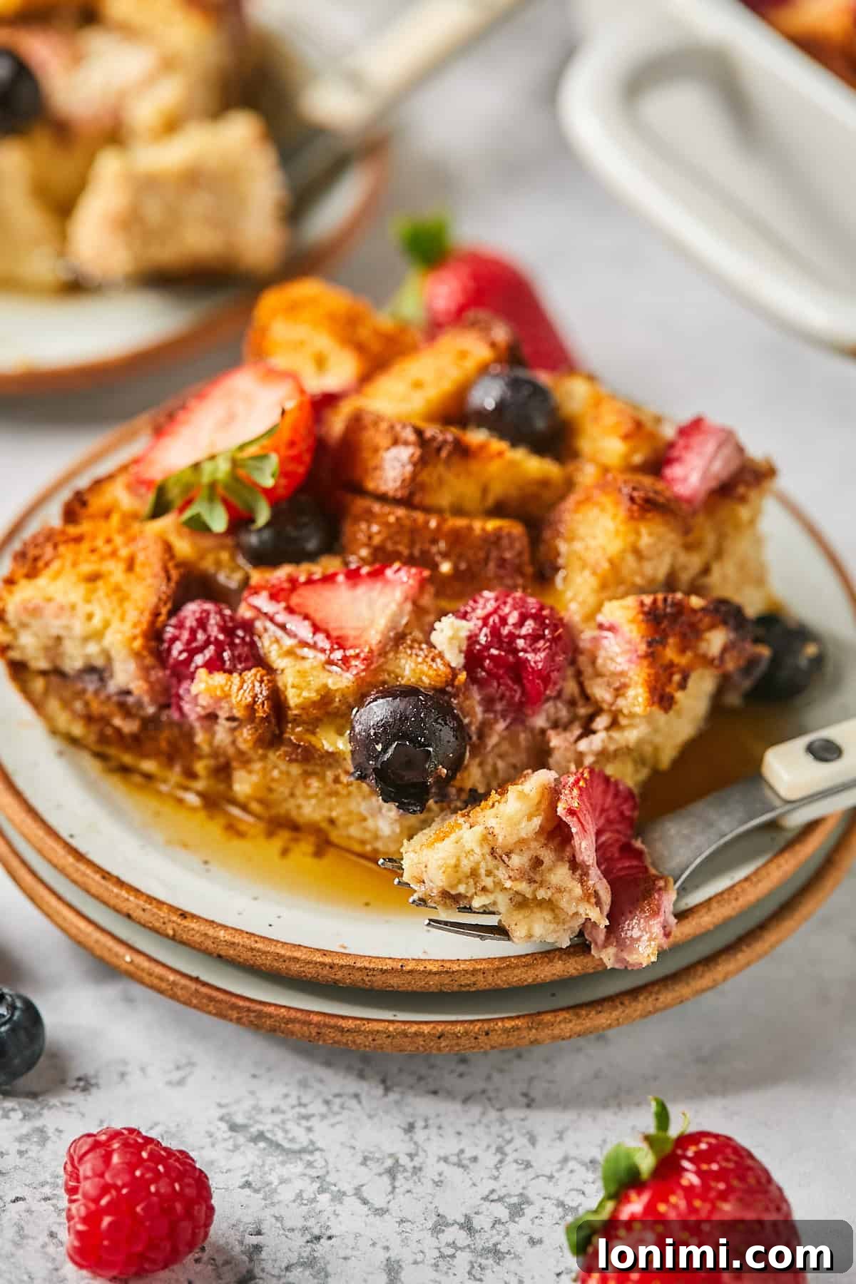 a fork with a bite of bread, syrup, and strawberries. 