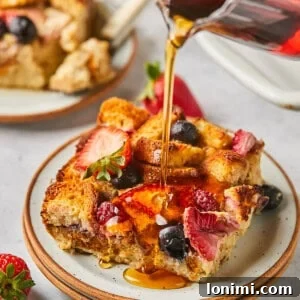 maple syrup being poured over protein french toast casserole with berries