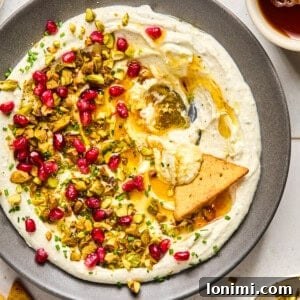 whipped feta with hot honey, pomegranates, and pistachios on a gray plate with a triangle pita chip in the middle