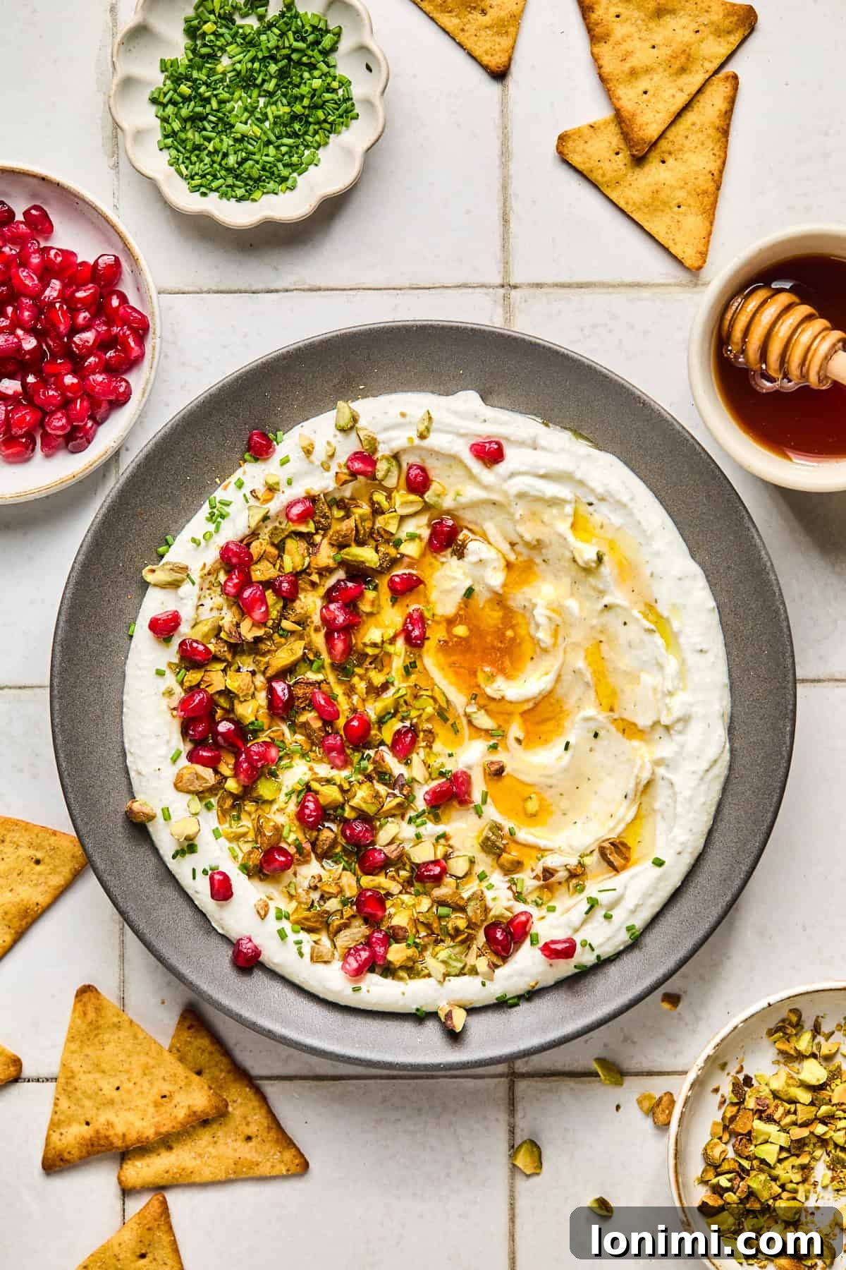 feta dip with toppings on a gray plate surrounded by ingredients and pita crackers