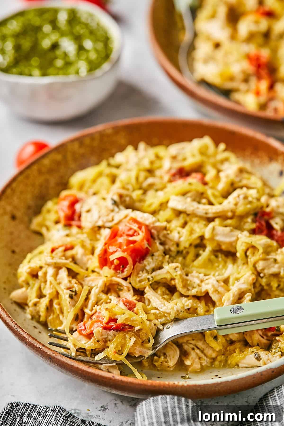 A perfectly portioned bowl of creamy Boursin chicken, mixed with spaghetti squash and blistered cherry tomatoes, garnished with fresh herbs.