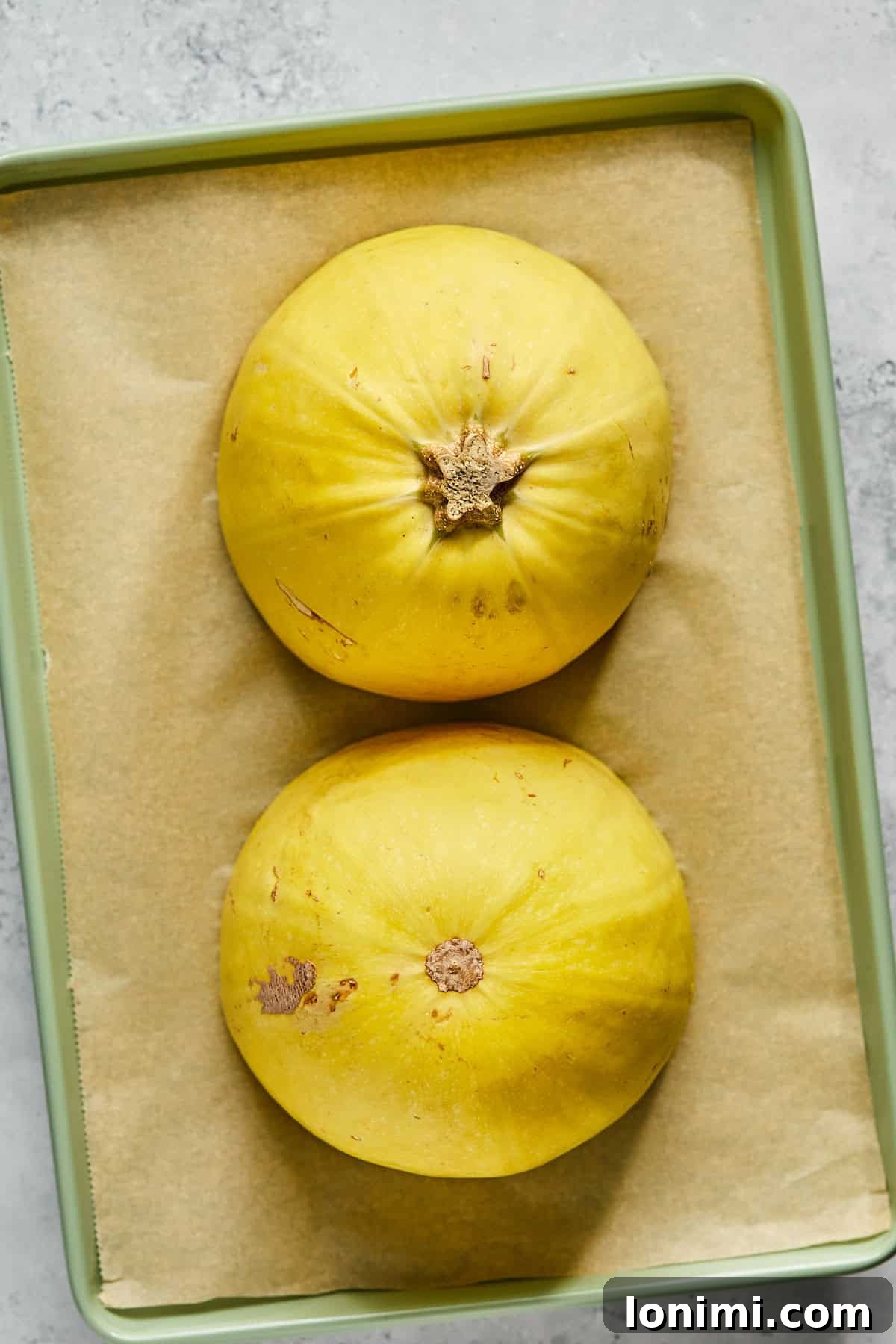 Two halves of spaghetti squash placed cut-side down on a parchment-lined baking sheet, prepared for roasting.