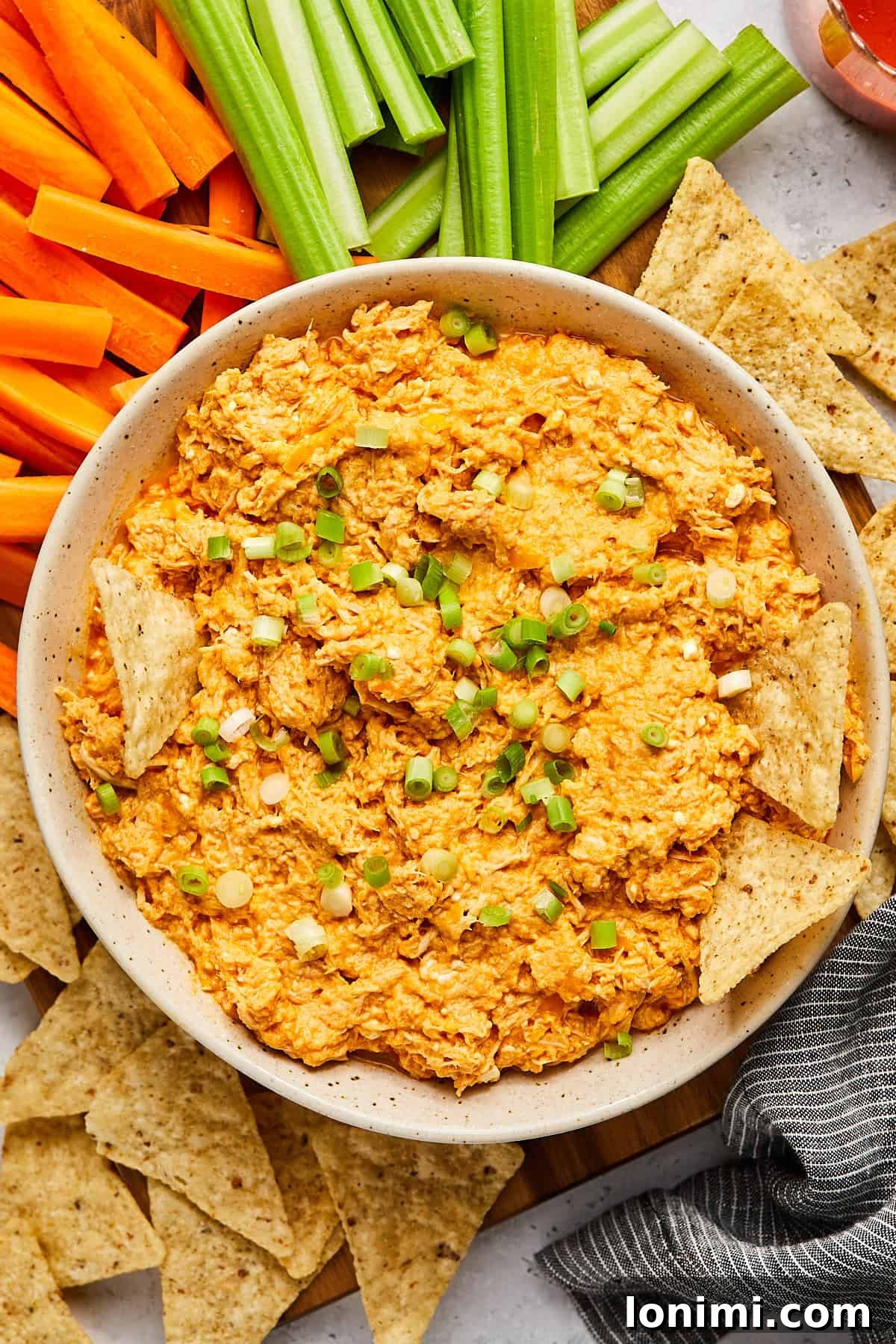 A bowl of high protein buffalo chicken dip, garnished with chopped green onions, ready to be served with crunchy dippers.