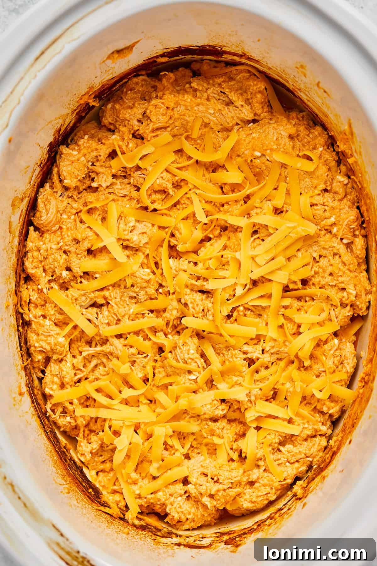 The buffalo chicken dip topped with a final layer of grated cheese, ready for melting.