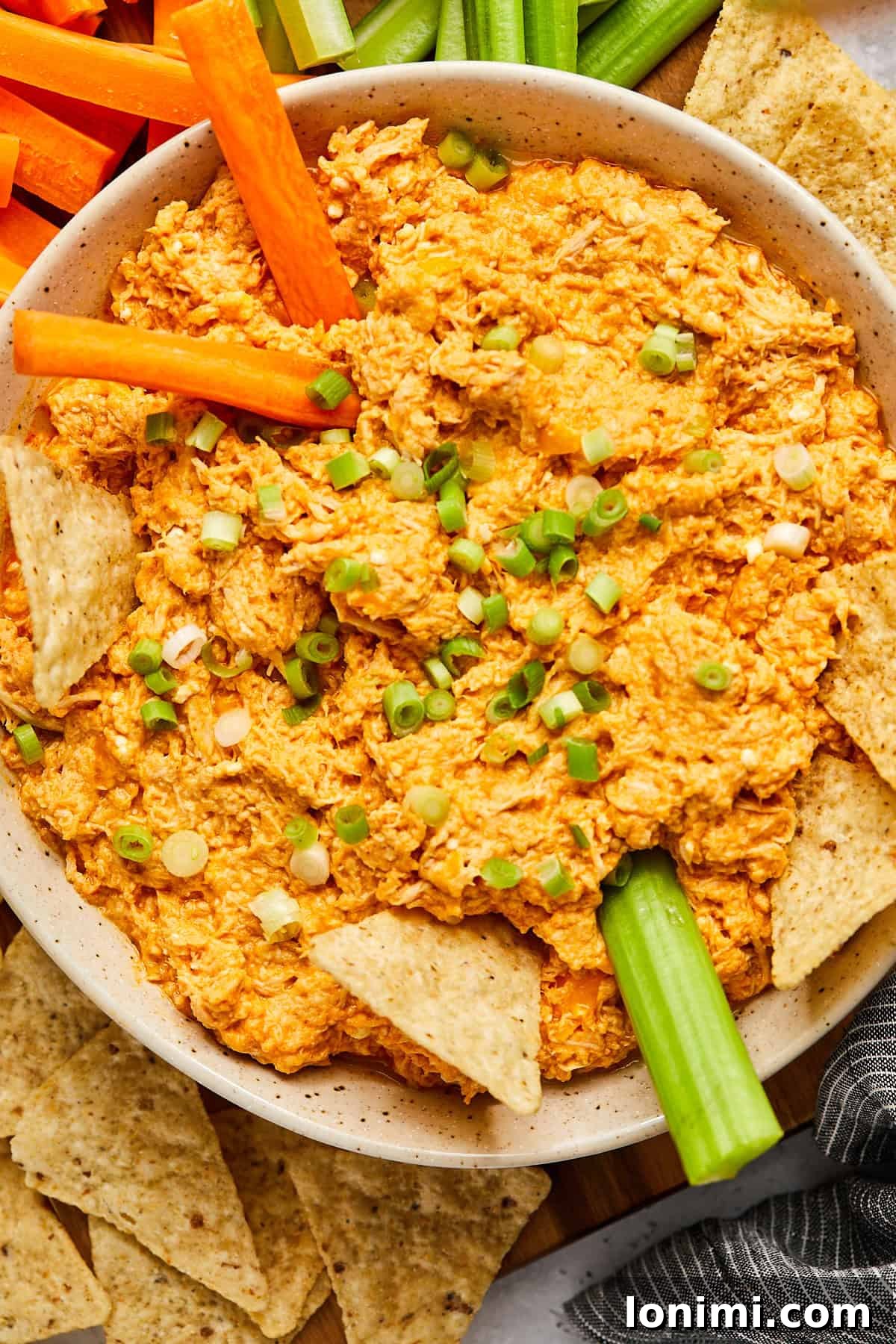 Crisp carrot sticks and celery sticks being dipped into a steaming bowl of slow cooker buffalo chicken dip, highlighting healthy dipping options.