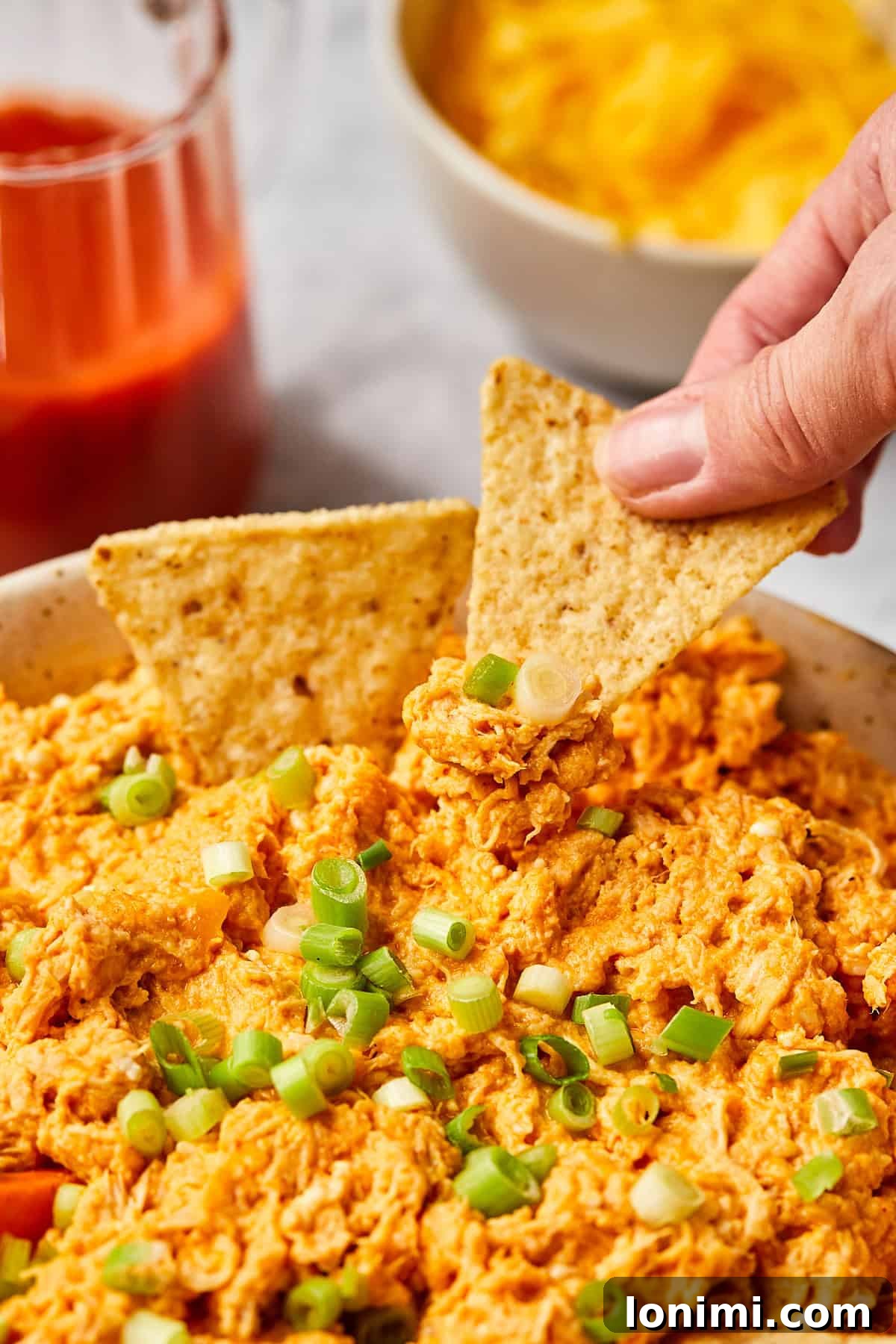 A hand reaching in with a tortilla chip to scoop up a generous portion of the creamy buffalo chicken dip.