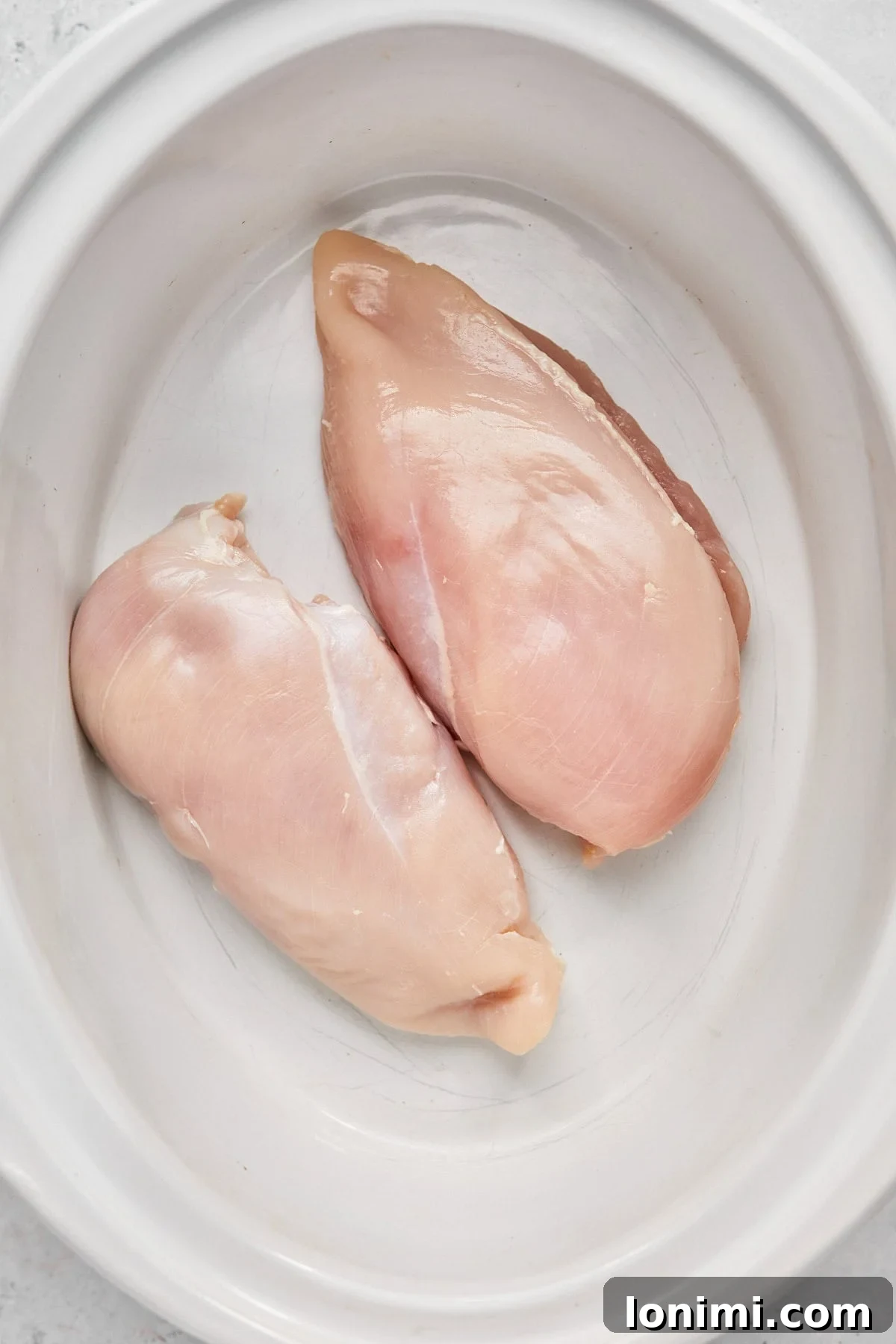 Raw chicken breasts nestled in the bottom of a slow cooker, ready for seasoning.