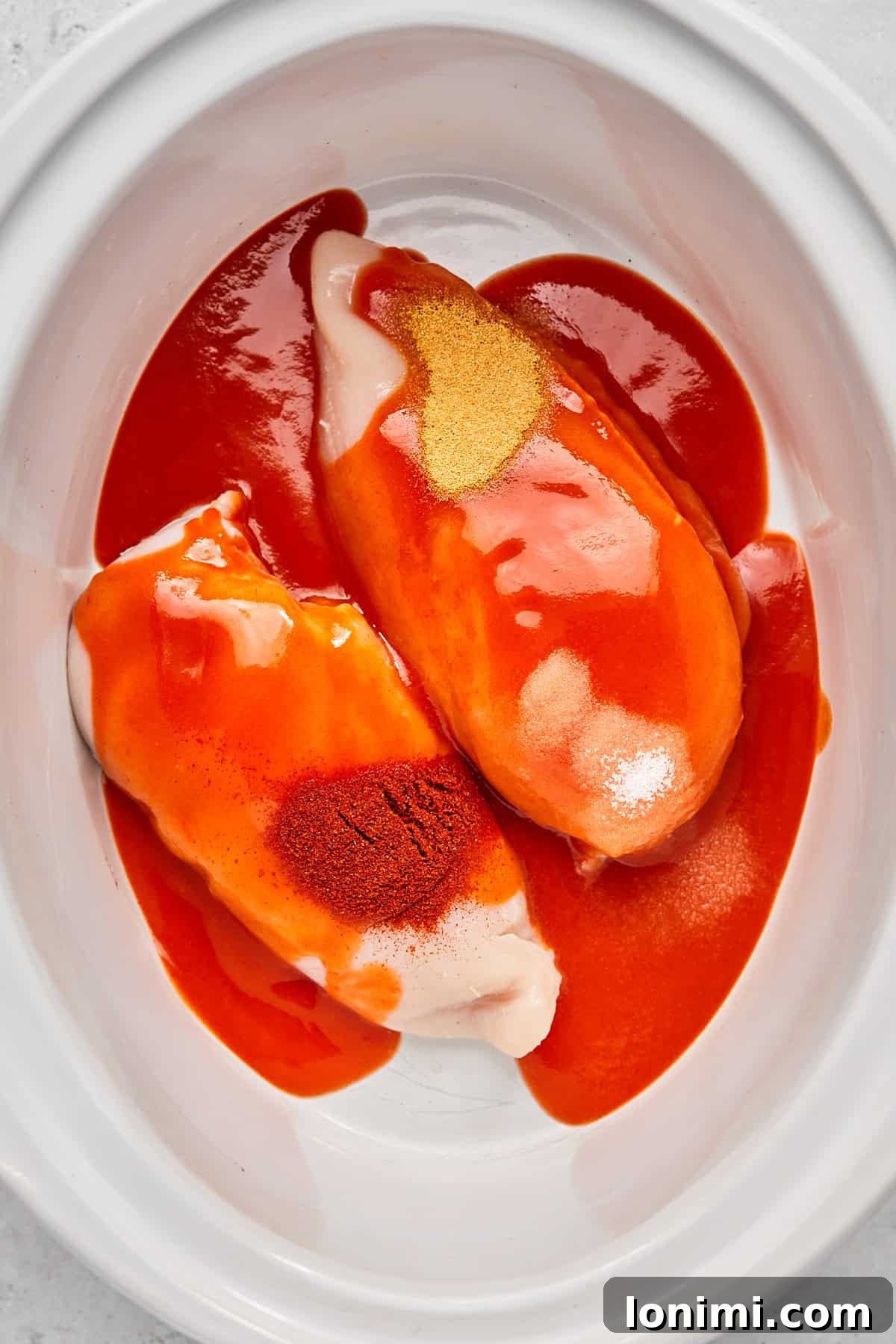 Chicken breasts in the slow cooker, generously covered with hot sauce and sprinkled with seasonings.