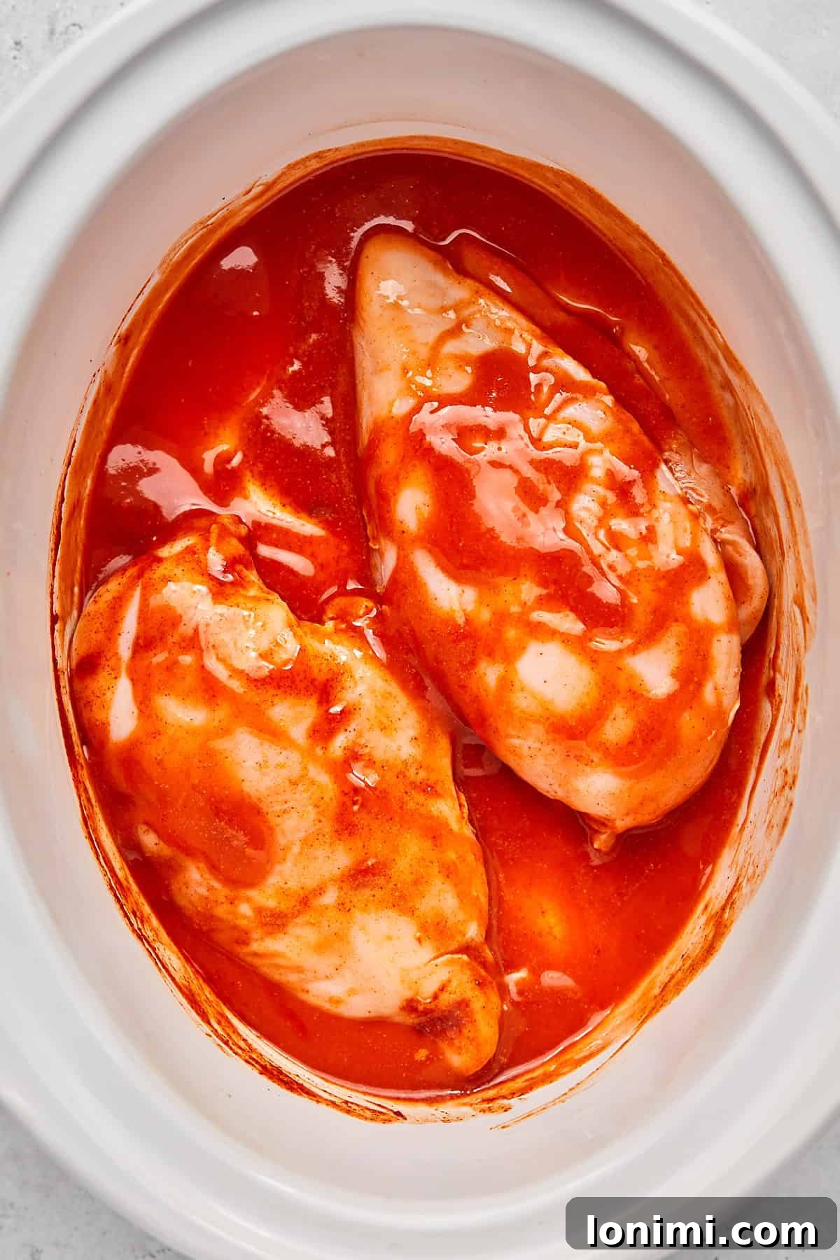 Raw chicken pieces coated thoroughly in buffalo sauce and seasonings within the crock pot.