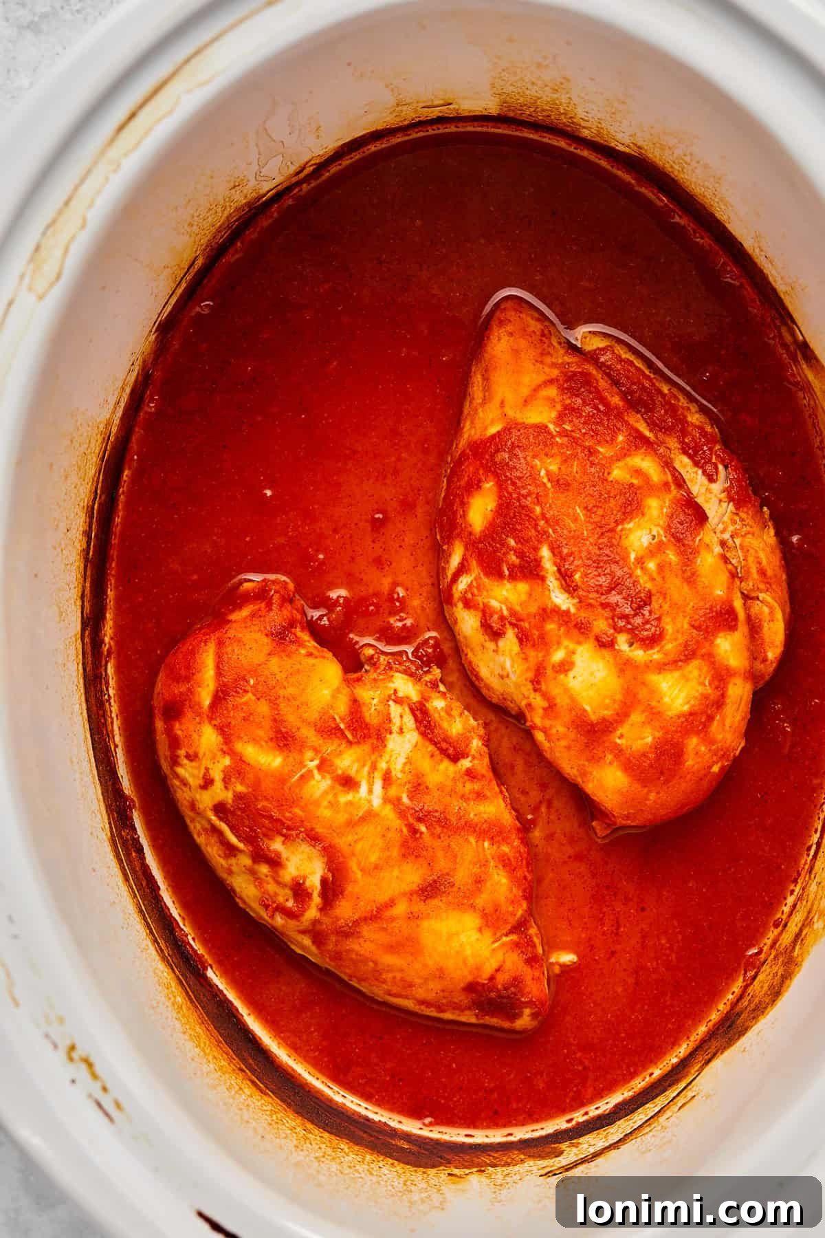 Cooked, tender chicken breasts simmering in rich buffalo sauce in the slow cooker.