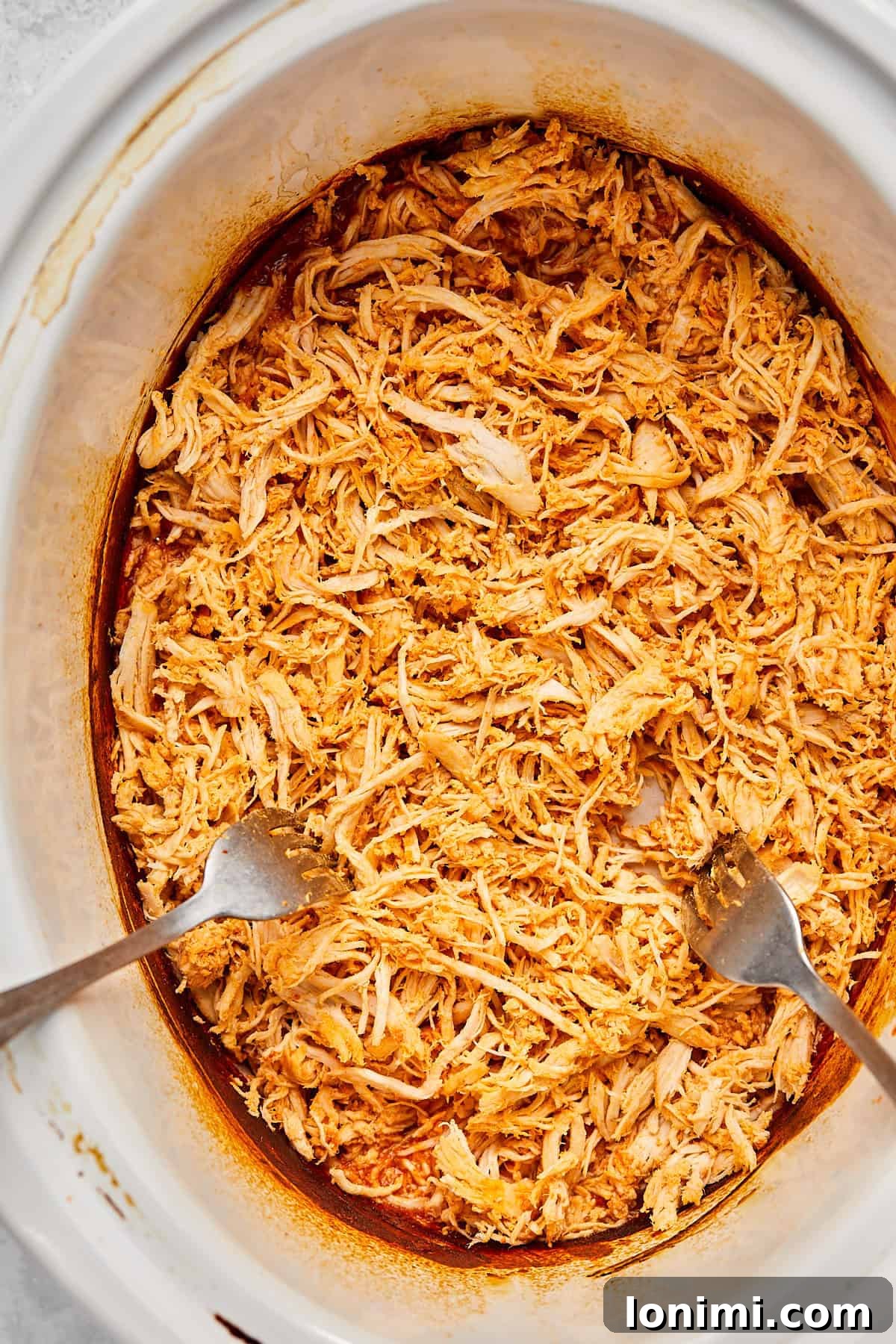 Cooked chicken being shredded effortlessly with two forks directly in the slow cooker.