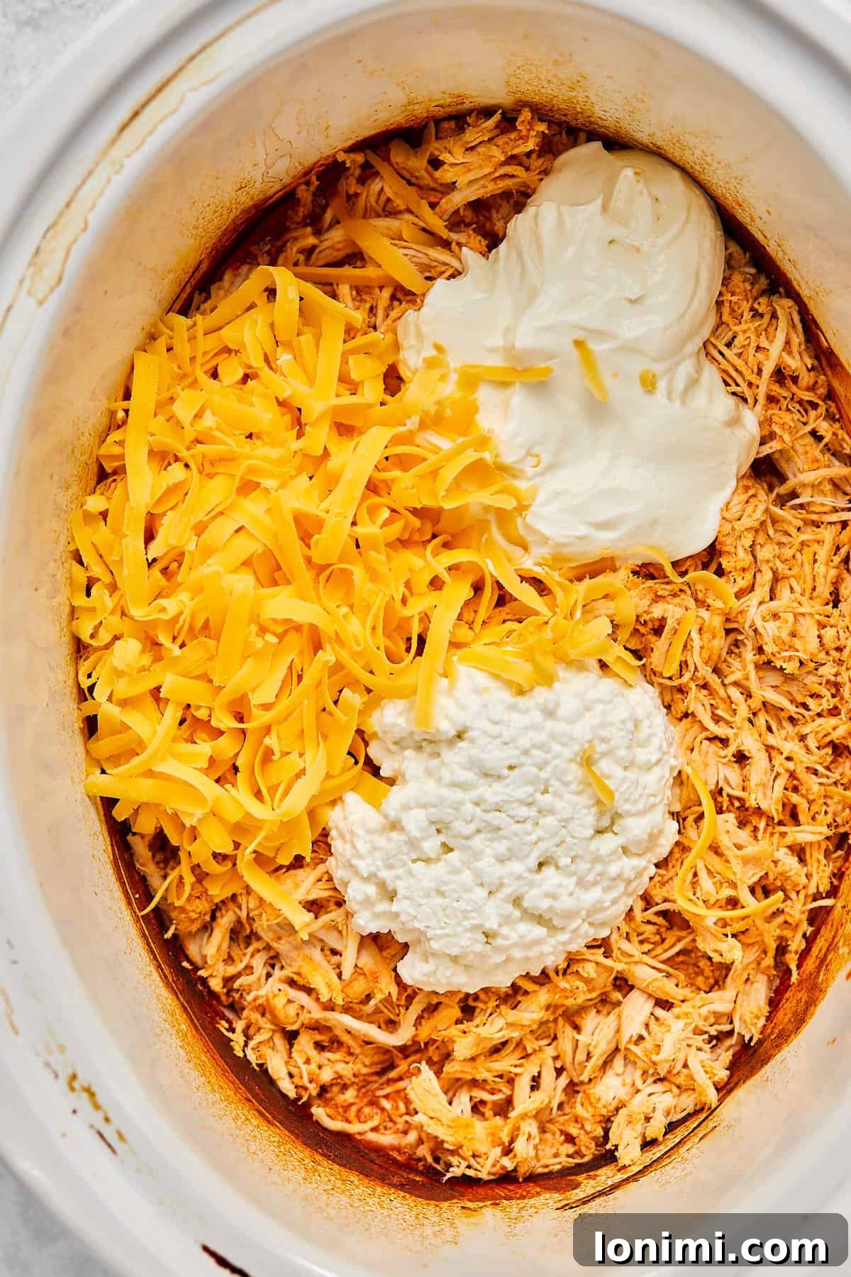 Adding cottage cheese, Greek yogurt, and a portion of shredded cheese to the shredded buffalo chicken.