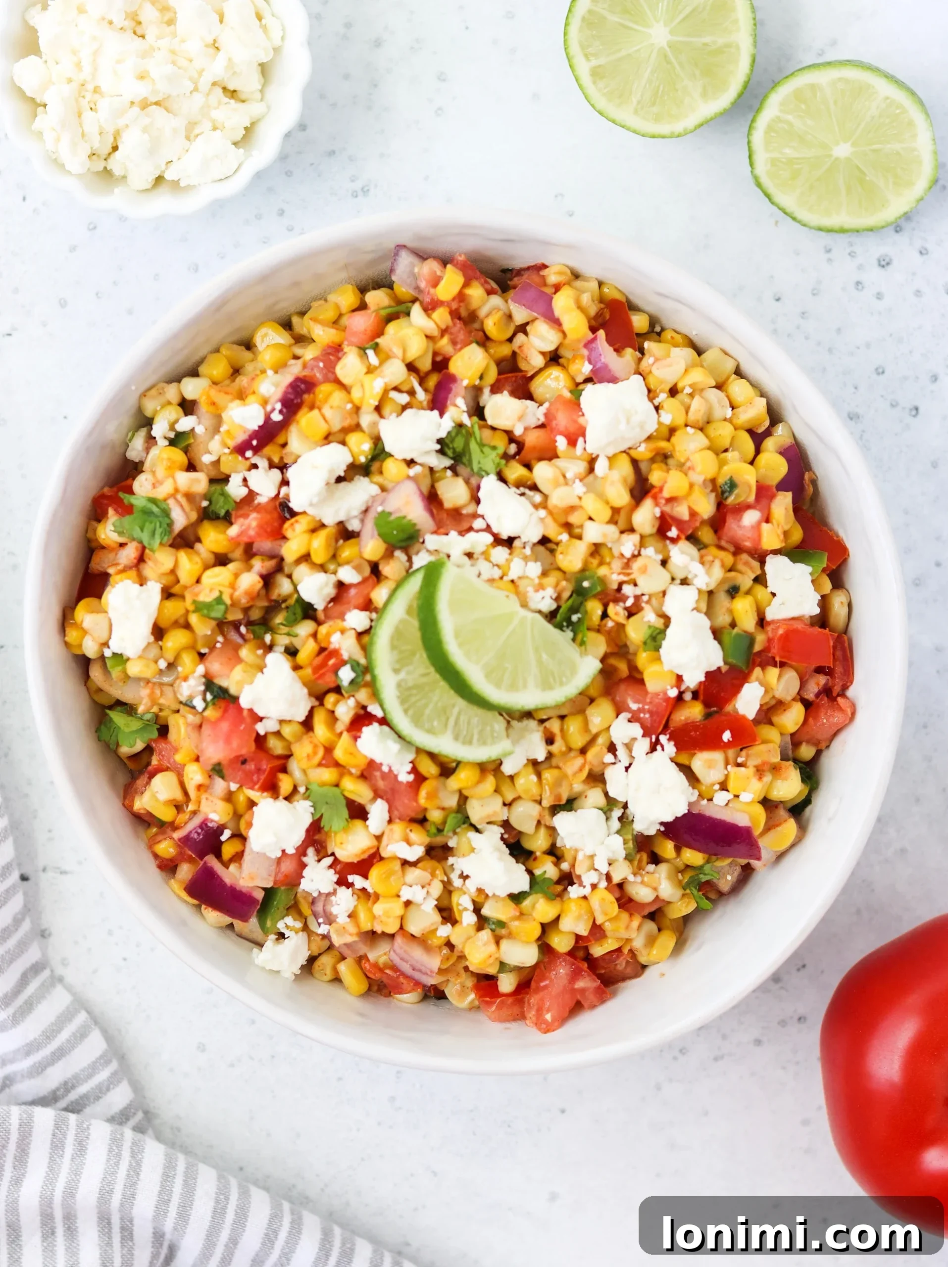 A large serving bowl filled with fresh Mexican Street Corn and Tomato Salad, ready to be enjoyed at a picnic or BBQ.