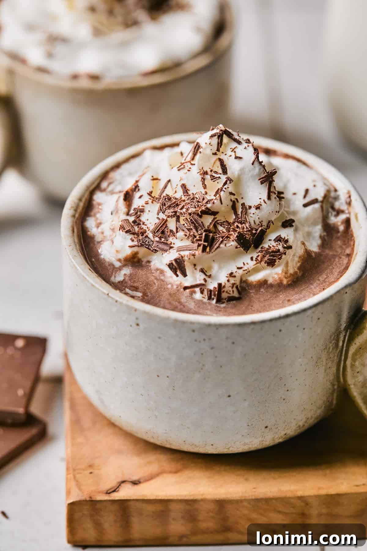 A steaming mug of rich protein hot chocolate, generously topped with fluffy whipped cream and delicate chocolate shavings, inviting a moment of cozy indulgence.