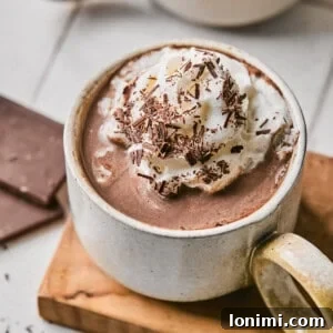 protein hot chocolate with whipped cream and chocolate shavings in a white mug on a wood plank