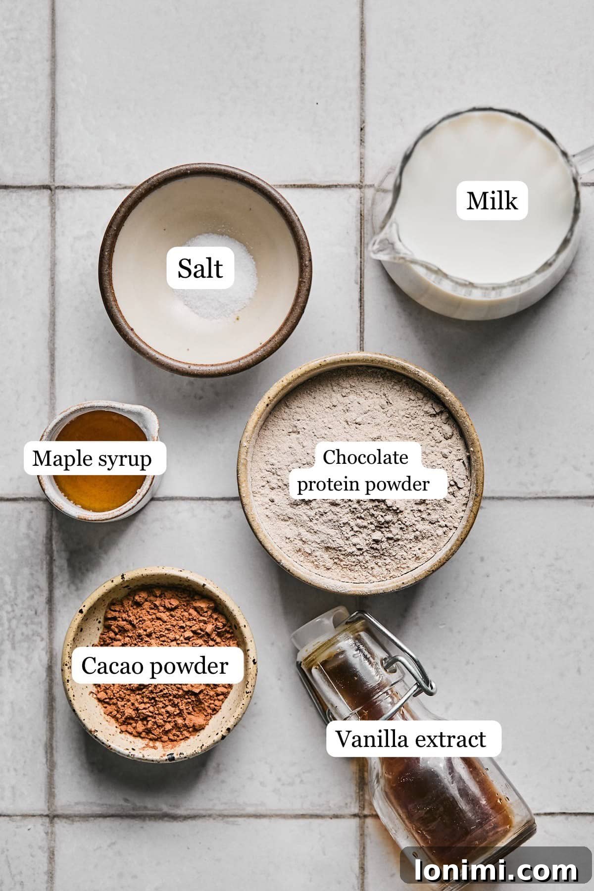 Individual bowls containing the key ingredients for protein hot chocolate: milk, chocolate protein powder, cacao powder, maple syrup, vanilla extract, and a pinch of sea salt.