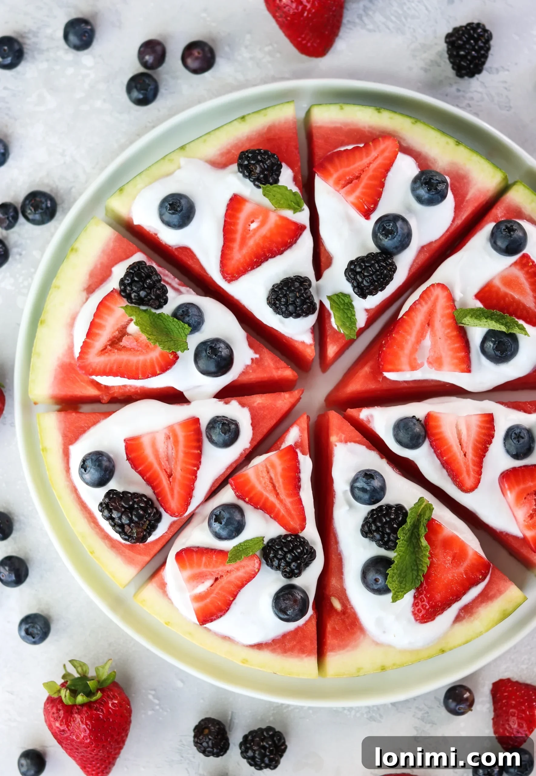 Individual slices of watermelon pizza arranged with homemade coconut whipped cream and a colorful array of fresh berries and mint leaves