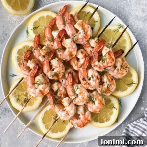 Grilled Garlic Butter Dill Shrimp on a white plate with fresh dill and lemon