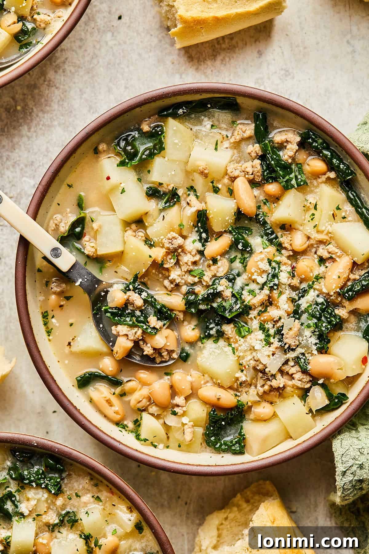 A steaming bowl of homemade Sausage Kale and White Bean Soup garnished with fresh parsley and a side of crusty baguette slices, ready to be enjoyed.