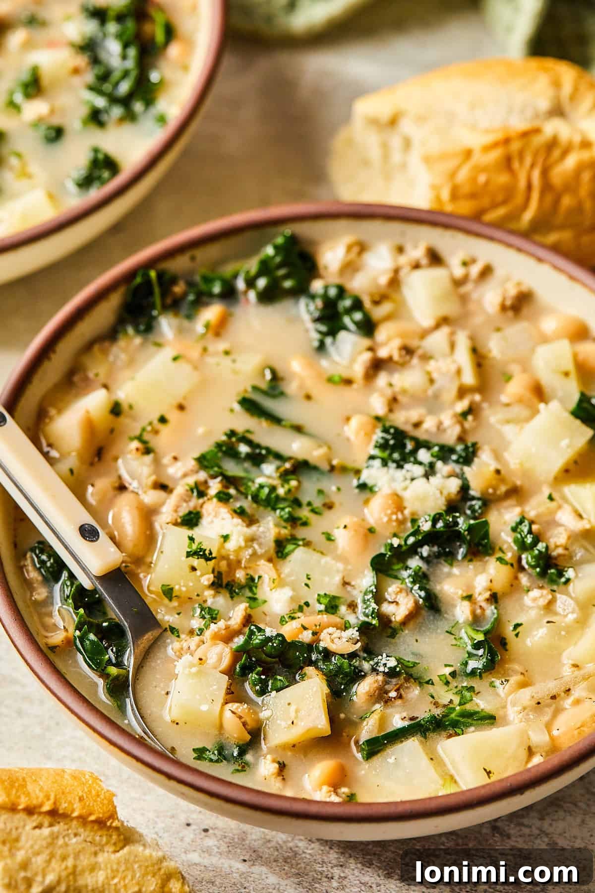 Close-up of a bowl of Sausage Kale and White Bean Soup with a spoon, highlighting the rich broth and textured ingredients.