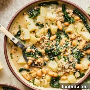 Sausage, kale and white bean soup in a bowl with a spoon surrounded by baguette slices