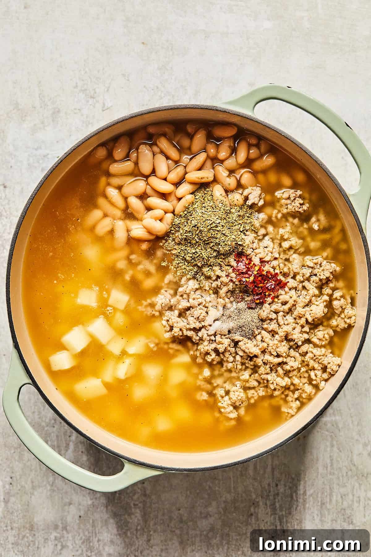 Ground turkey, cannellini beans, cubed potatoes, chicken broth, and spices simmering in a pot.