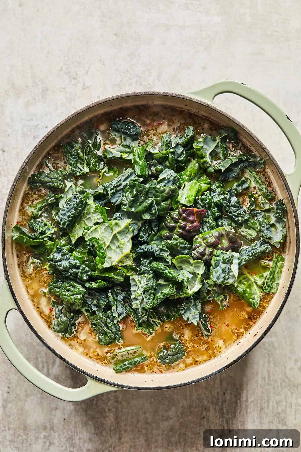 Fresh kale being stirred into a pot of hot soup, wilting into the broth.