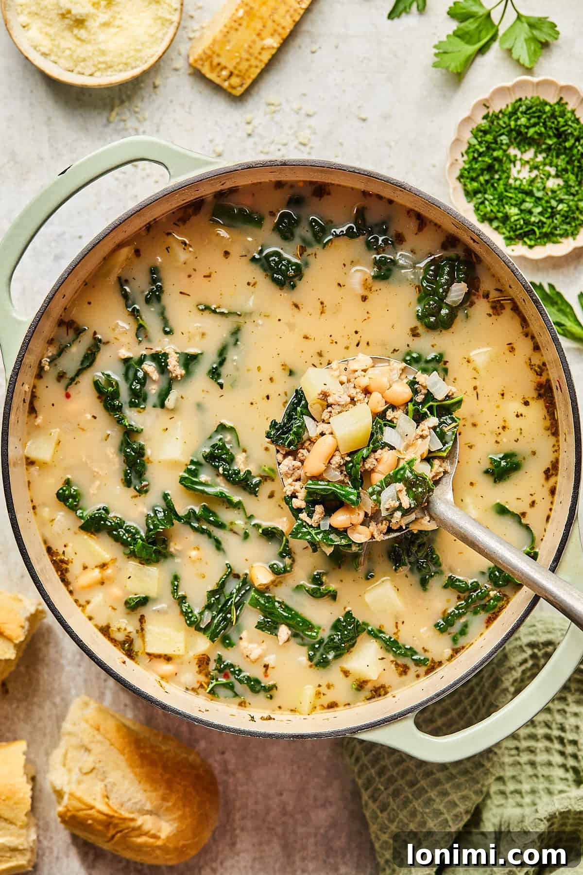 A large pot of creamy Sausage Kale and White Bean Soup with a ladle, ready to be served.