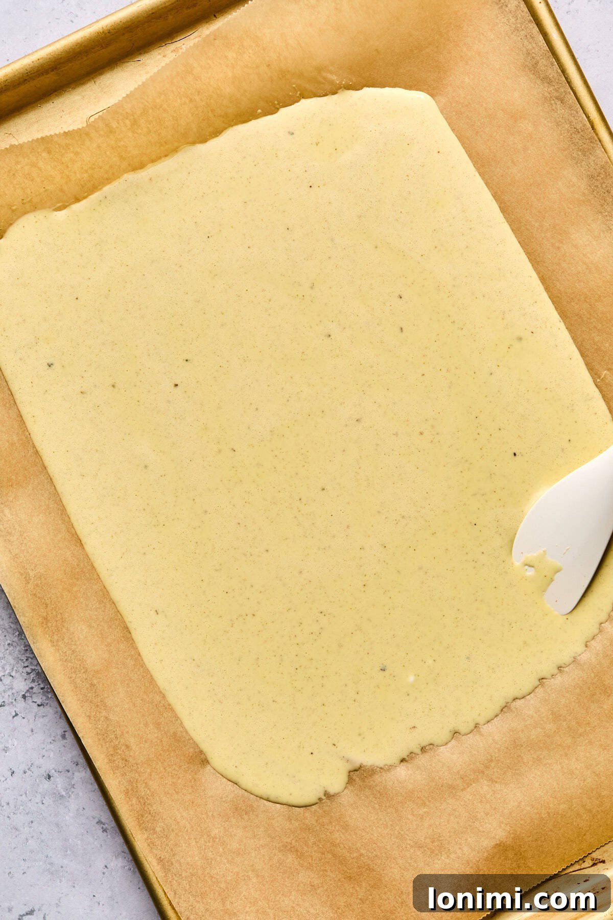 cottage cheese flatbread liquid ingredients on a parchment lined baking sheet with a white spatula