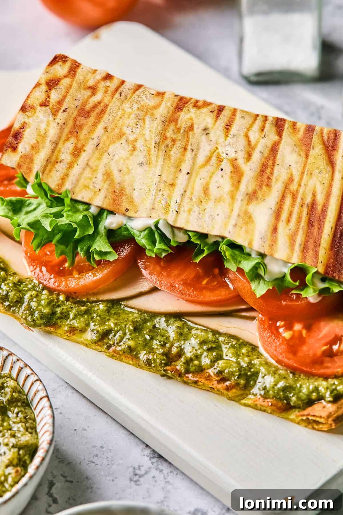 a side view of a flatbread sandwich with lettuce, tomato, turkey and pesto