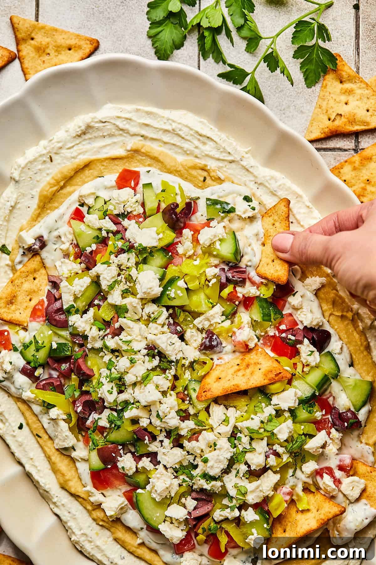 Effortless Mediterranean Layered Feta Dip 11 A hand dipping triangle chips into dip